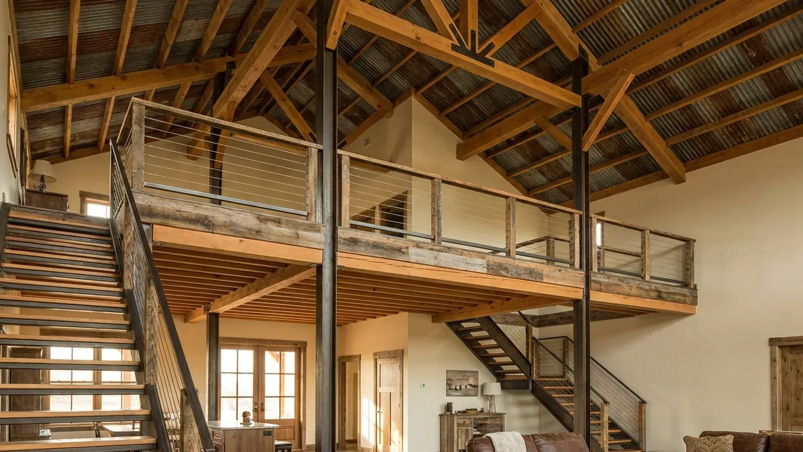 A barndominium great room with an open loft level and railing built over part of the room, reached by an open staircase.